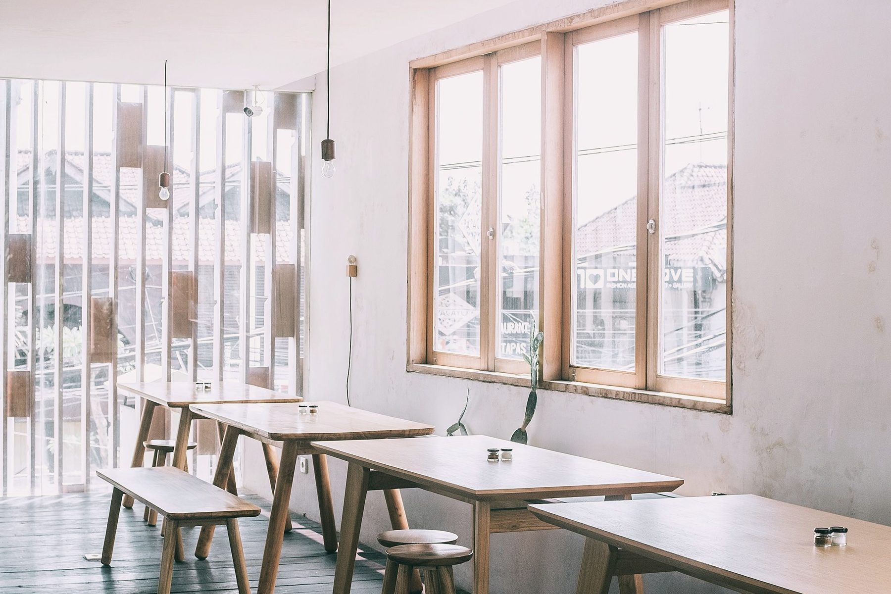 Long pale wooden tables and benches in a white room with tall windows.