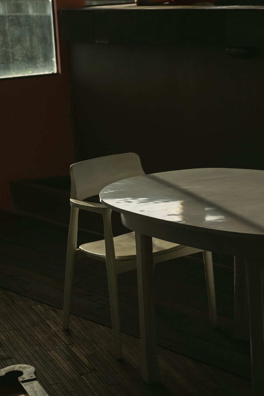 A cream table and chair beside a window in a dark room, a band of light across the tabletop.