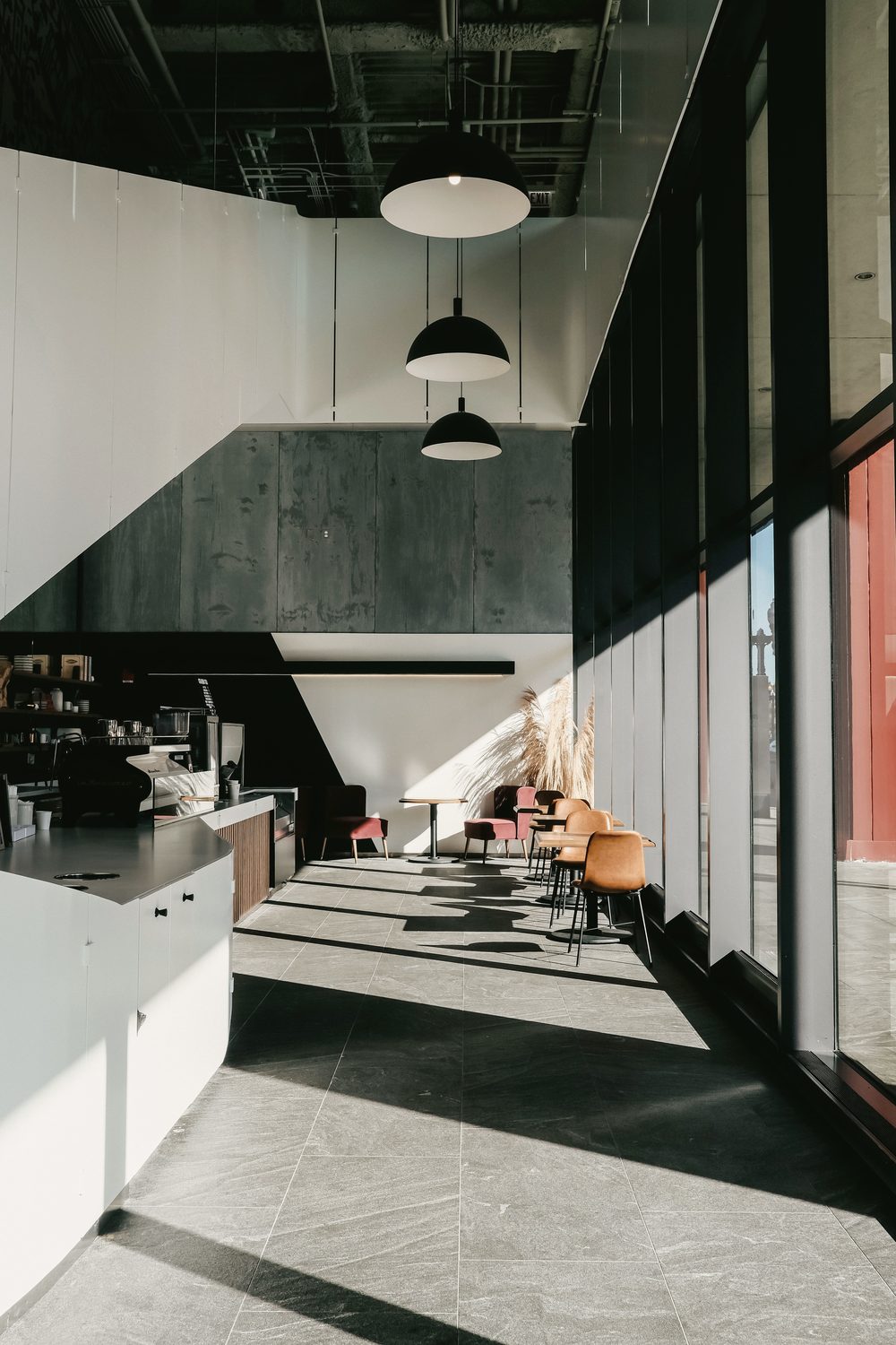 A café counter seen from the seating, hard sunlight through full-height glazing.