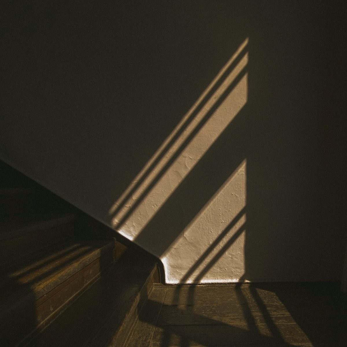 A wooden stair edge against a plaster wall, striped with light from a window.