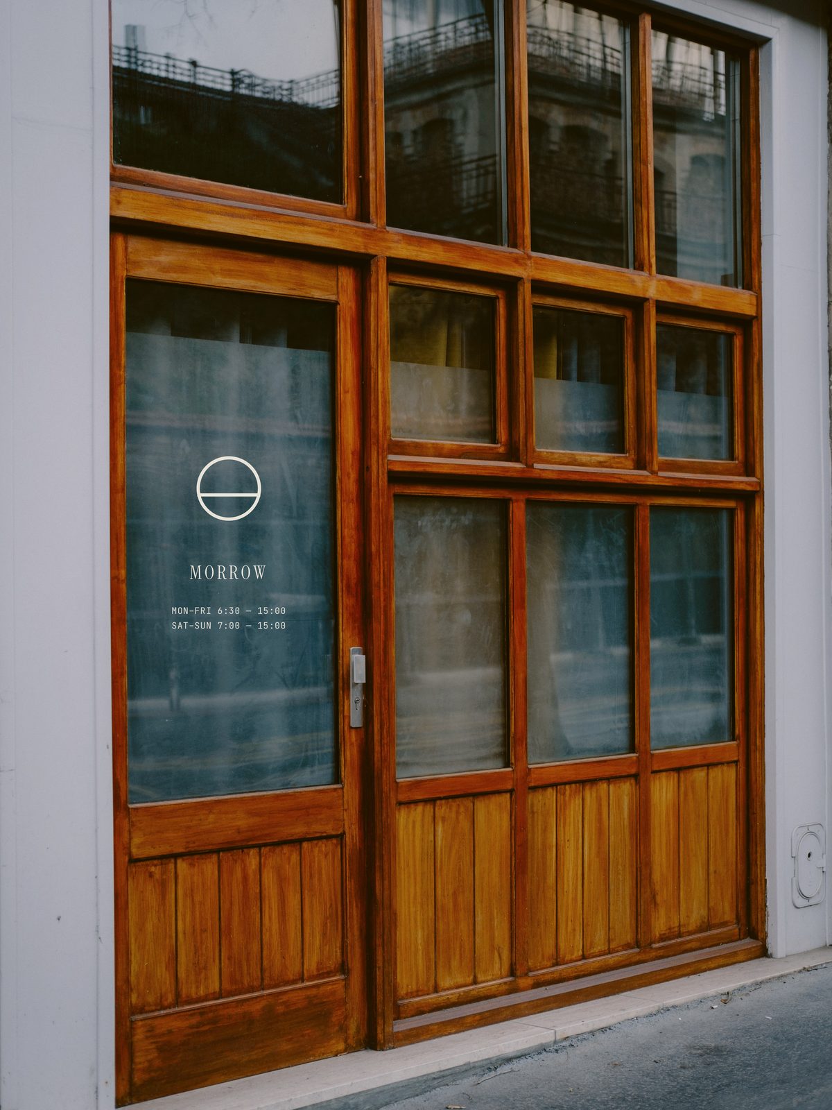 A café storefront: oak-framed glazing and door set into a white plaster wall, the Morrow mark and hours on the door glass.
